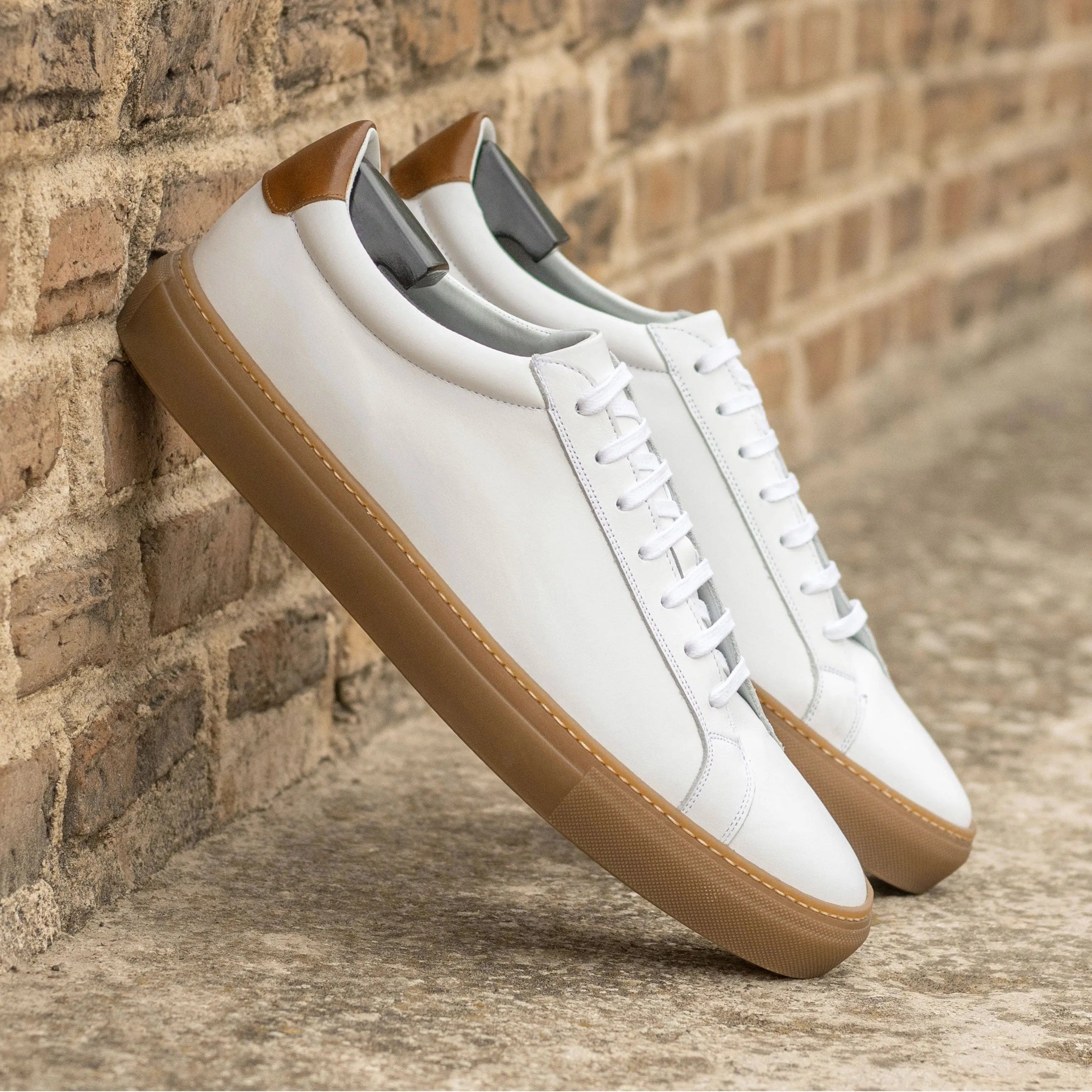 White leather Conquest Low Kick Sneakers with brown soles, ideal for stylish comfort