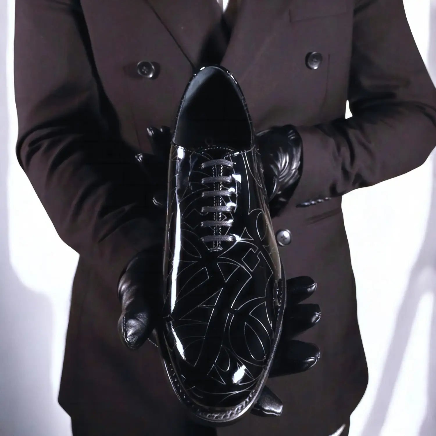Black patent leather oxford shoe with intricate silver-toned geometric and floral embossed detailing.