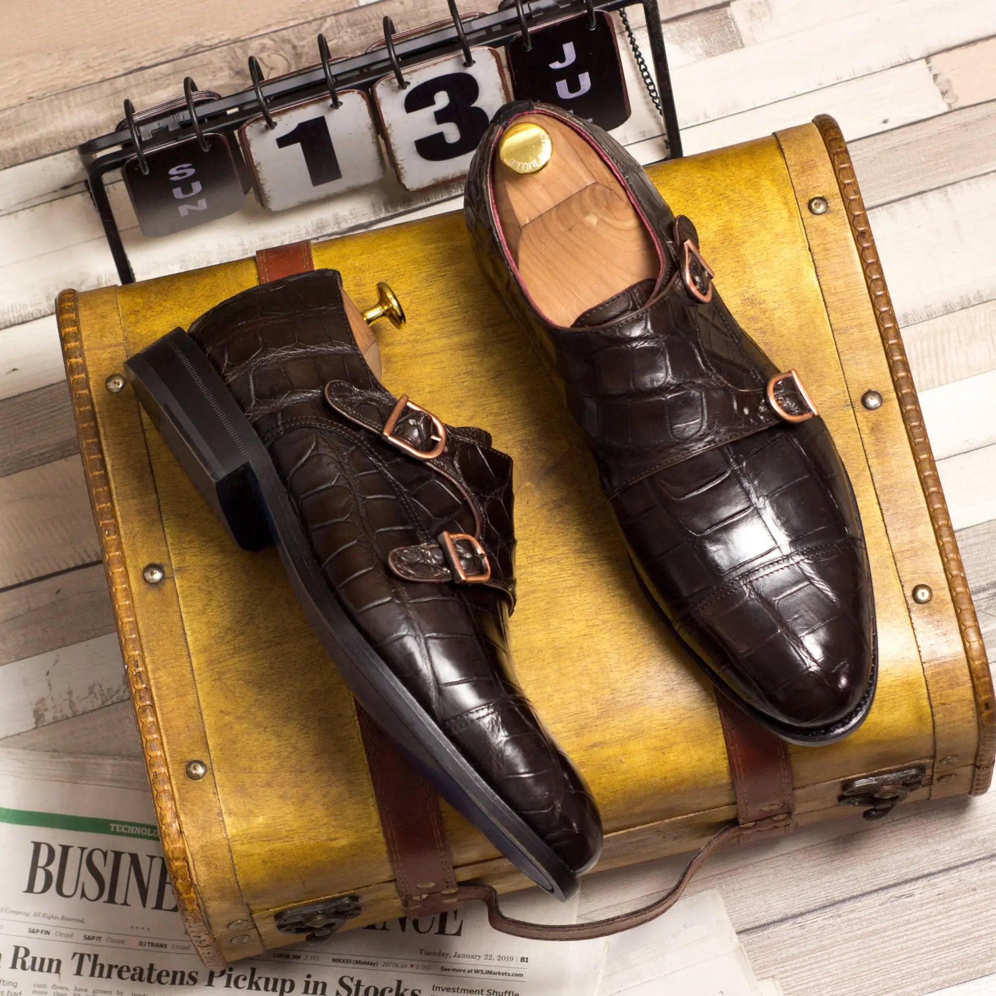 Brown crocodile skin monk strap shoes with gold buckles and leather soles.